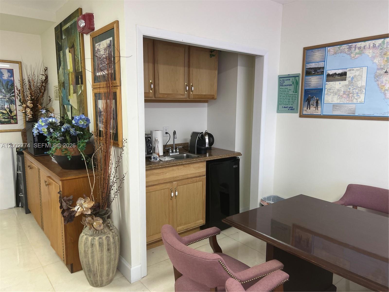 A small kitchenette with wooden cabinets and a black mini-fridge sits beside a dining area — 1720 Harrison St, Hollywood FL 33020, HOLLYWOOD, FL