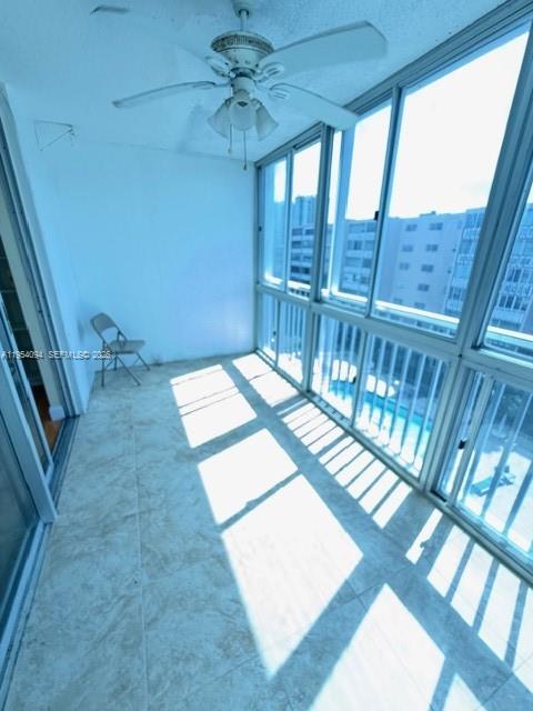 A sunroom with tile flooring, a ceiling fan, and large windows overlooking a city building — 319 NE 14th Ave # 607, Hallandale Beach FL 33009, HALLANDALE BEACH, FL