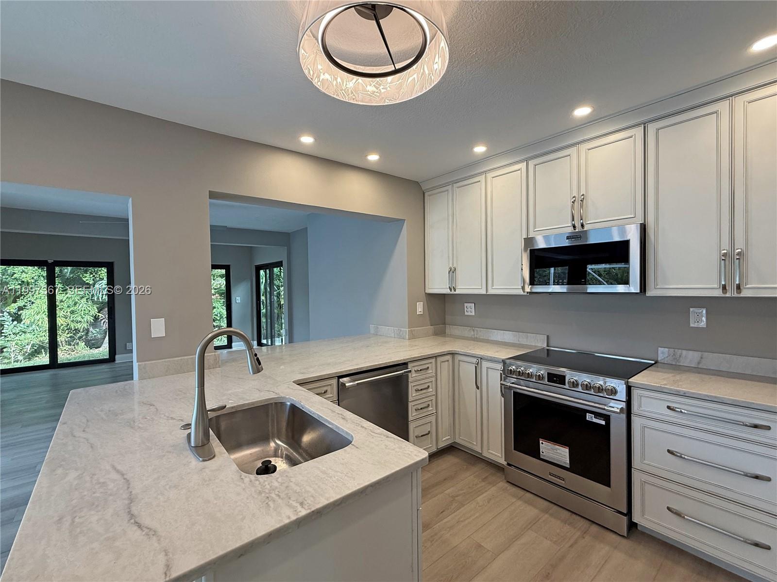 A modern kitchen features white cabinetry, stainless steel appliances, and a marble-topped island with sink — 410 SW 56th Ave, Plantation FL 33317, PLANTATION, FL