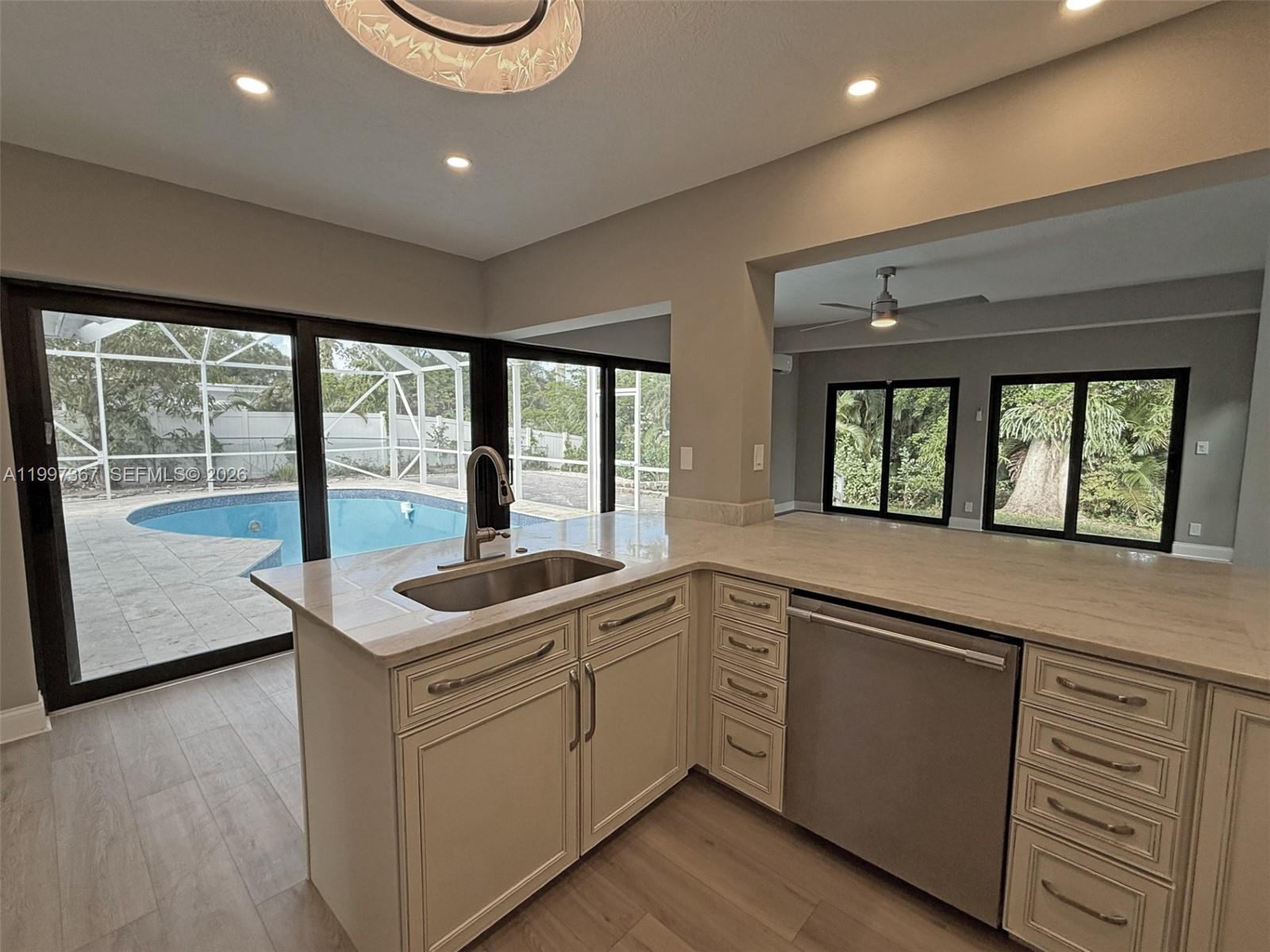 A kitchen with light cabinets and stone countertops overlooks a backyard swimming pool — 410 SW 56th Ave, Plantation FL 33317, PLANTATION, FL