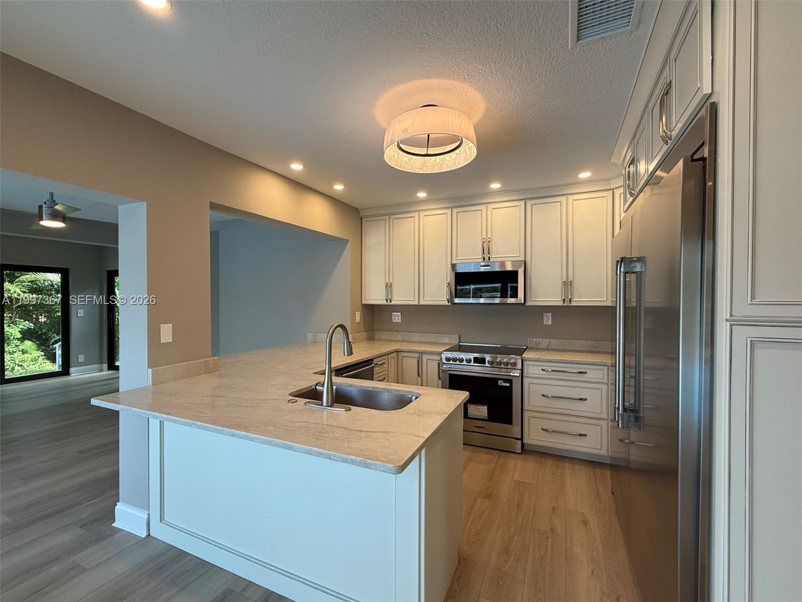 A kitchen features white cabinets, stainless steel appliances, a peninsula with a sink, and wood-look flooring — 410 SW 56th Ave, Plantation FL 33317, PLANTATION, FL
