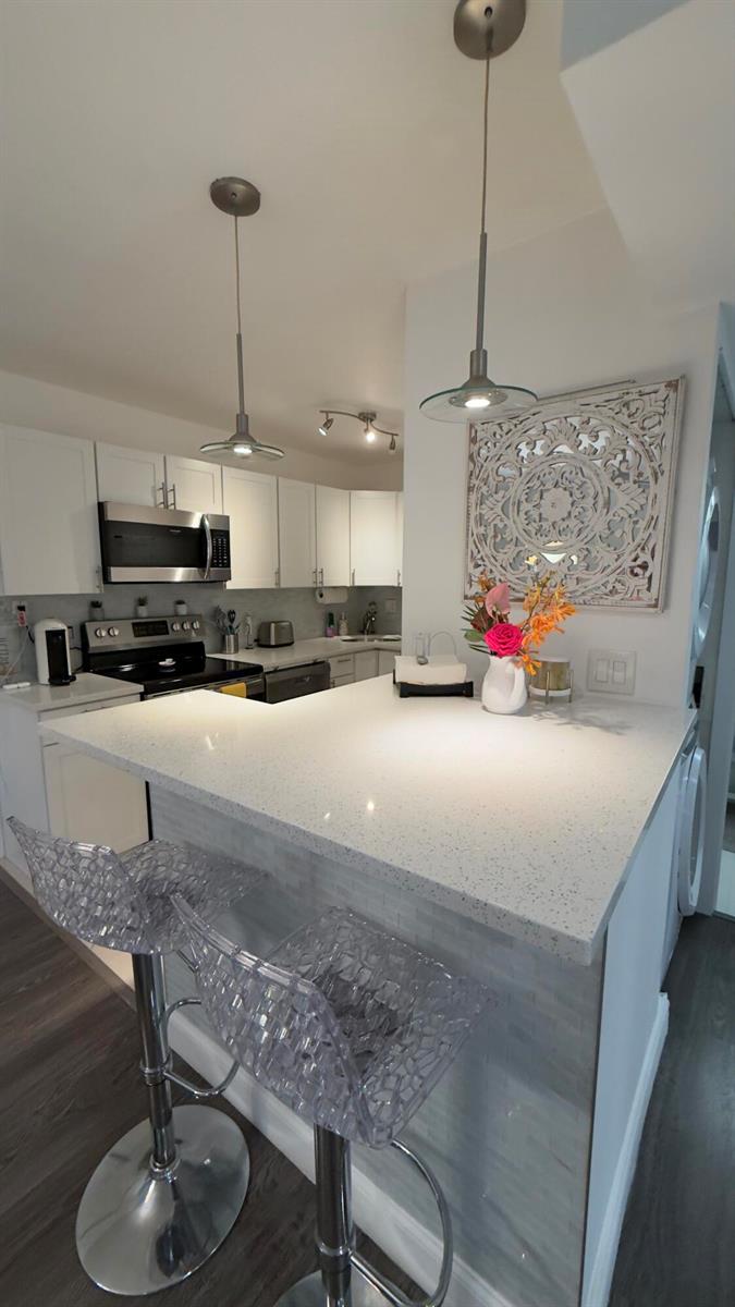 A kitchen features white cabinets, quartz countertops, a breakfast bar, and two clear acrylic stools — 702 SE 2nd Avenue SE # 405, Deerfield Beach FL 33441, DEERFIELD BEACH, FL