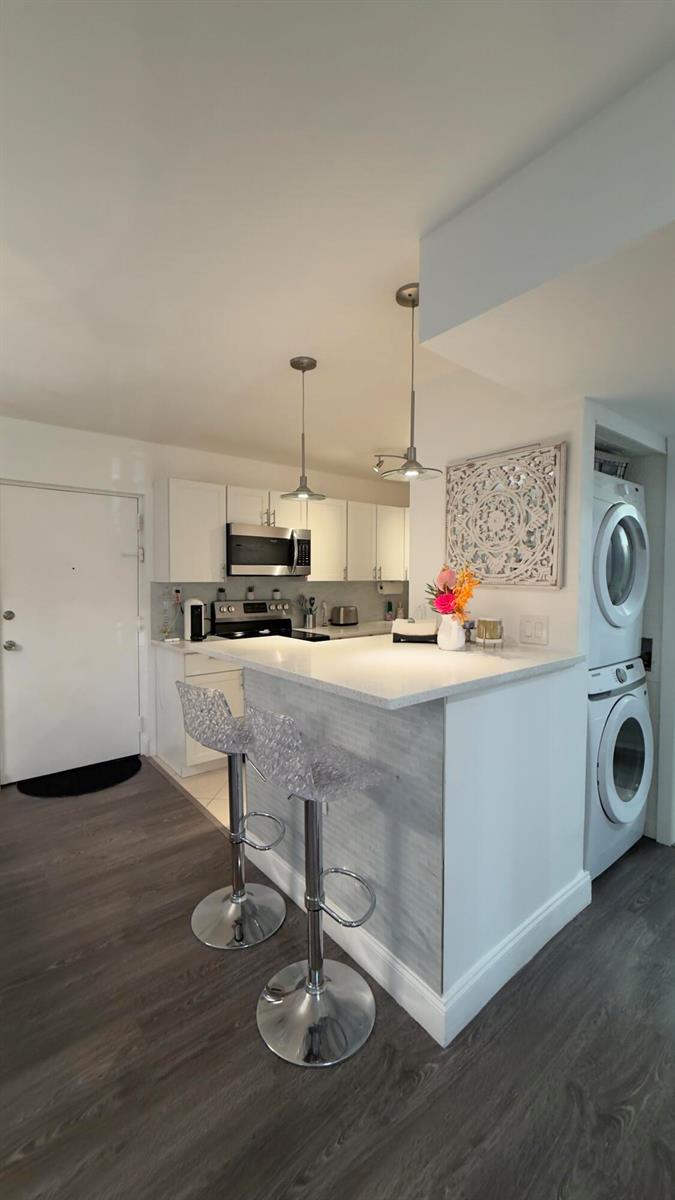 A kitchen with white cabinets, a breakfast bar with two stools, and a stacked washer-dryer — 702 SE 2nd Avenue SE # 405, Deerfield Beach FL 33441, DEERFIELD BEACH, FL