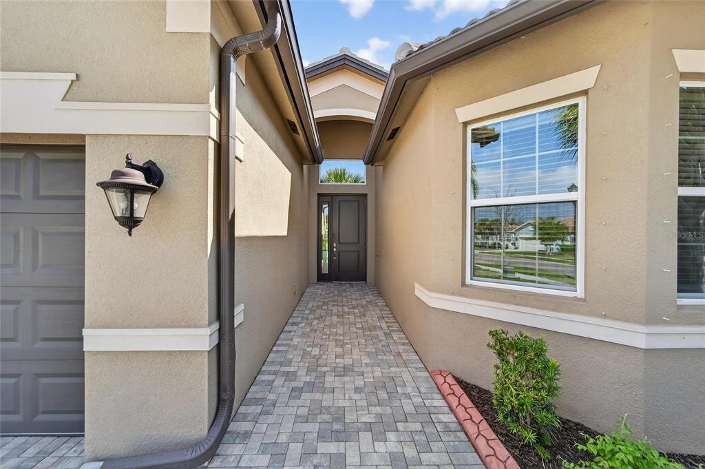 A paved walkway leads to the dark front door of a tan stucco house — 15512 CORONA DEL MAR DRIVE, WIMAUMA, FL