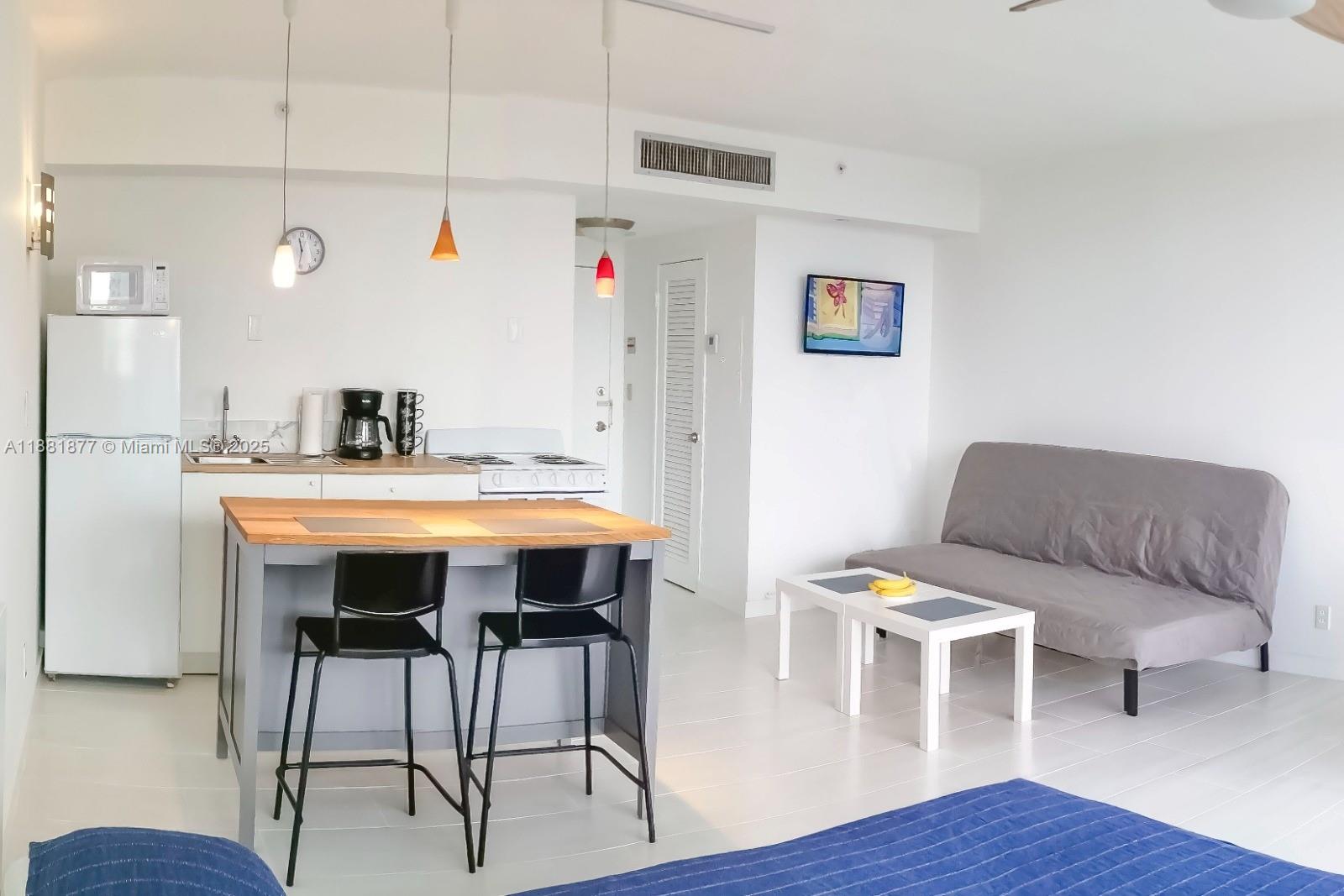 A studio apartment features a kitchen with a breakfast bar, a sofa, and white flooring — 1720 Harrison St # 10F, Hollywood FL 33020, HOLLYWOOD, FL