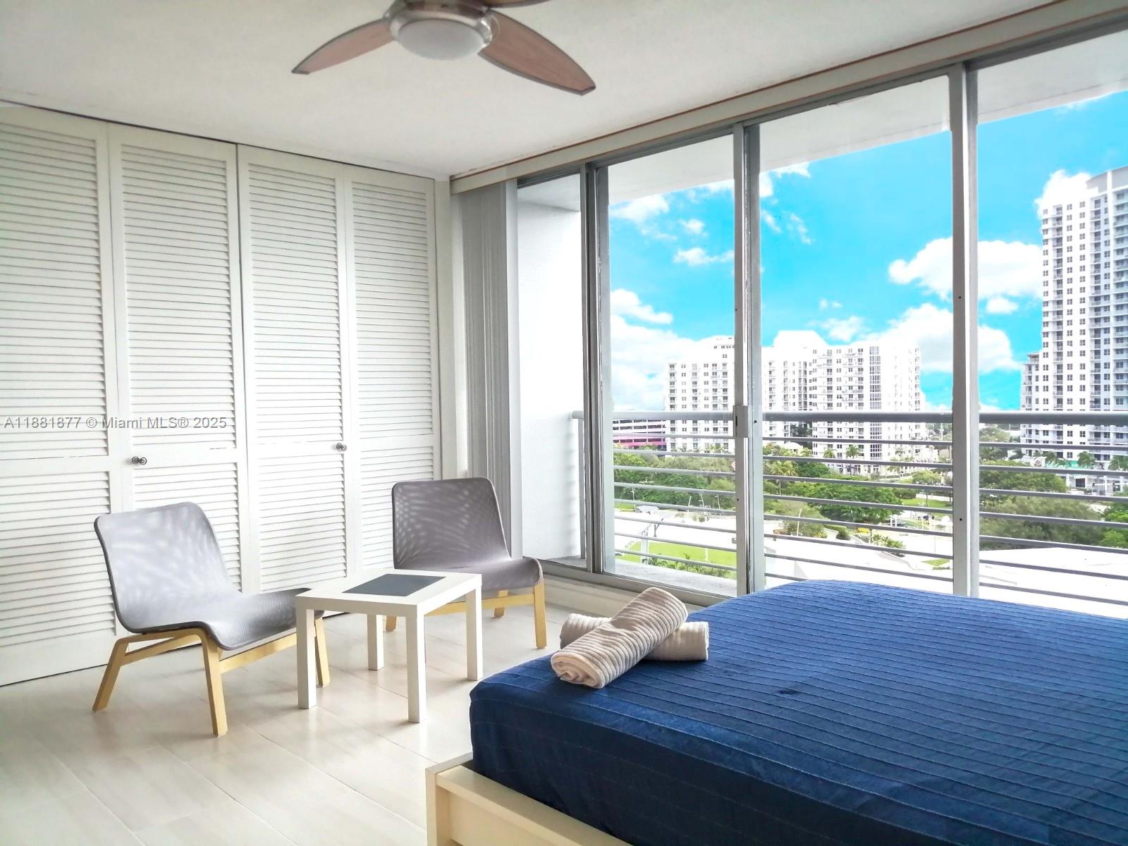 A bedroom features a blue bed, two chairs, a small table, and a balcony view — 1720 Harrison St # 10F, Hollywood FL 33020, HOLLYWOOD, FL