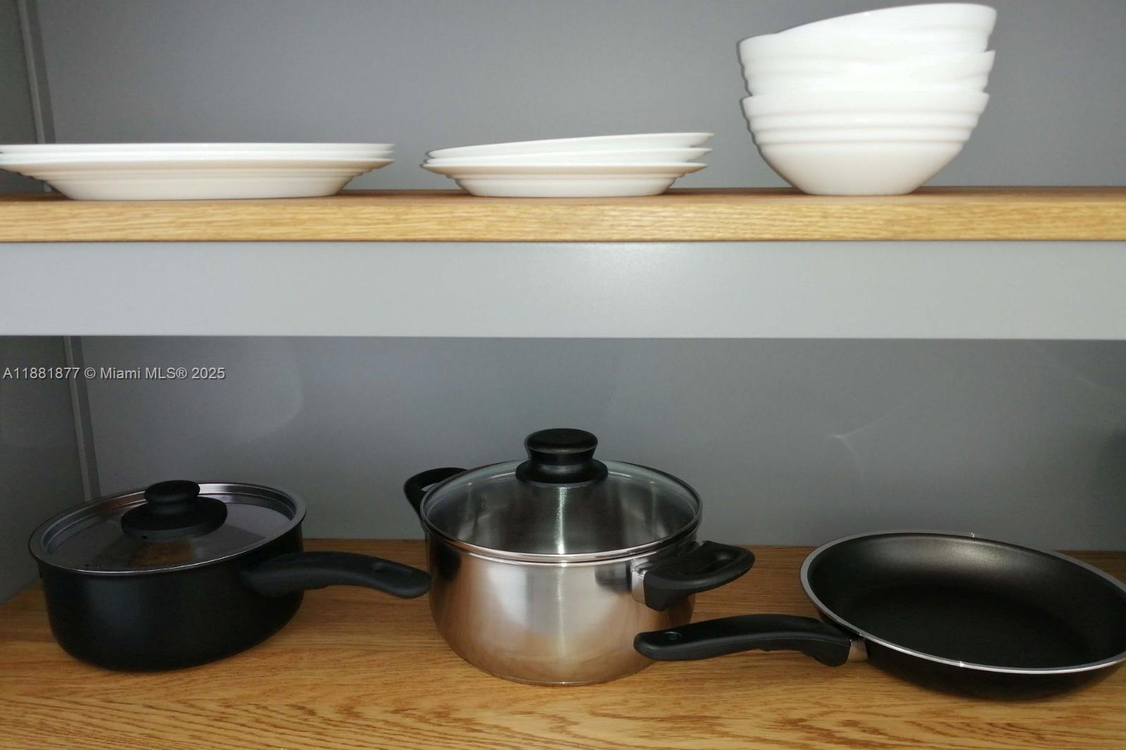 A wooden shelf holds white plates and bowls above a shelf with cookware — 1720 Harrison St # 10F, Hollywood FL 33020, HOLLYWOOD, FL