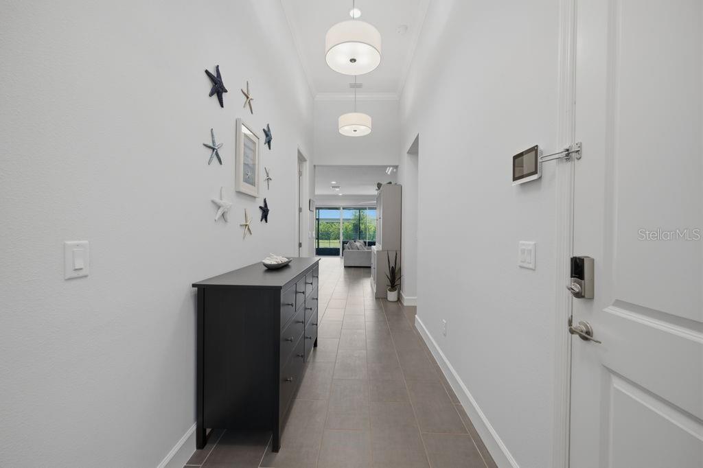 A hallway with tile flooring, a black dresser, and wall-mounted starfish decor leads to a living area — 3101 MALTA AVENUE, WESLEY CHAPEL, FL