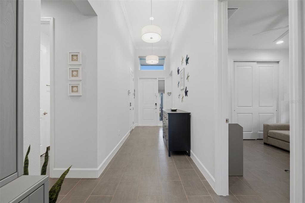 A bright hallway features light gray walls, tile flooring, a pendant light, and a dark console — 3101 MALTA AVENUE, WESLEY CHAPEL, FL