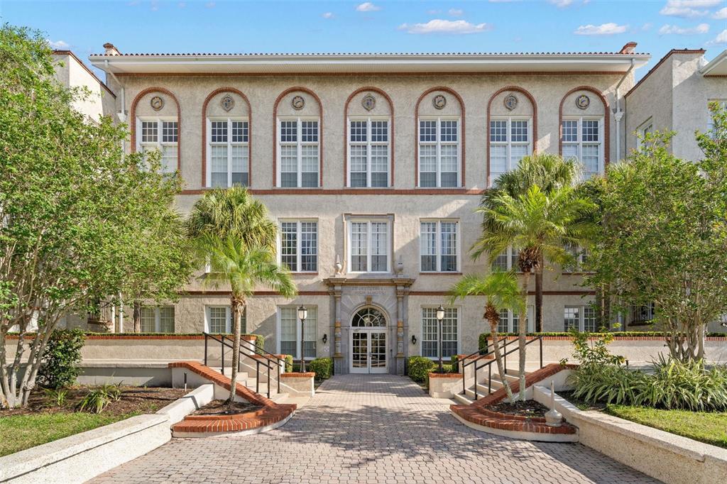 A multi-story building with a stucco facade, arched entrance, and symmetrical windows behind a walkway — 701 MIRROR LAKE DRIVE N UNIT 201, ST PETERSBURG, FL