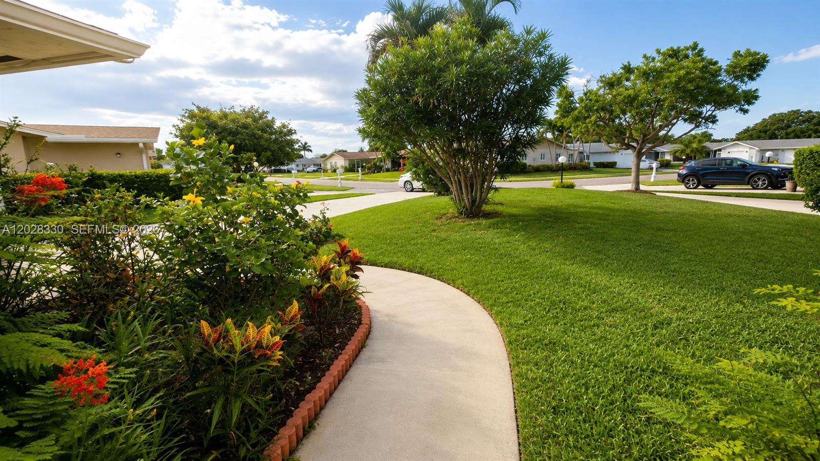 A concrete walkway curves through a grassy front yard with landscaping and a parked car — 13190 Via Vesta, Delray Beach FL 33484, DELRAY BEACH, FL