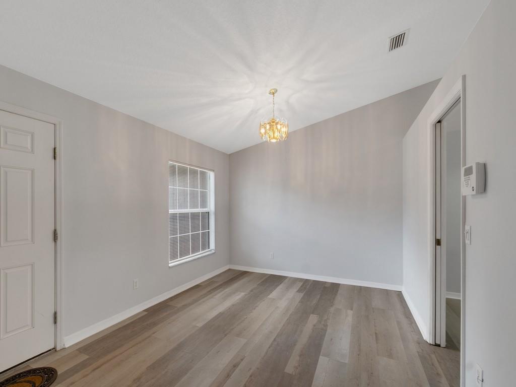 An empty room with light gray walls, wood-look flooring, a vaulted ceiling, and a chandelier — VERO BEACH, FL