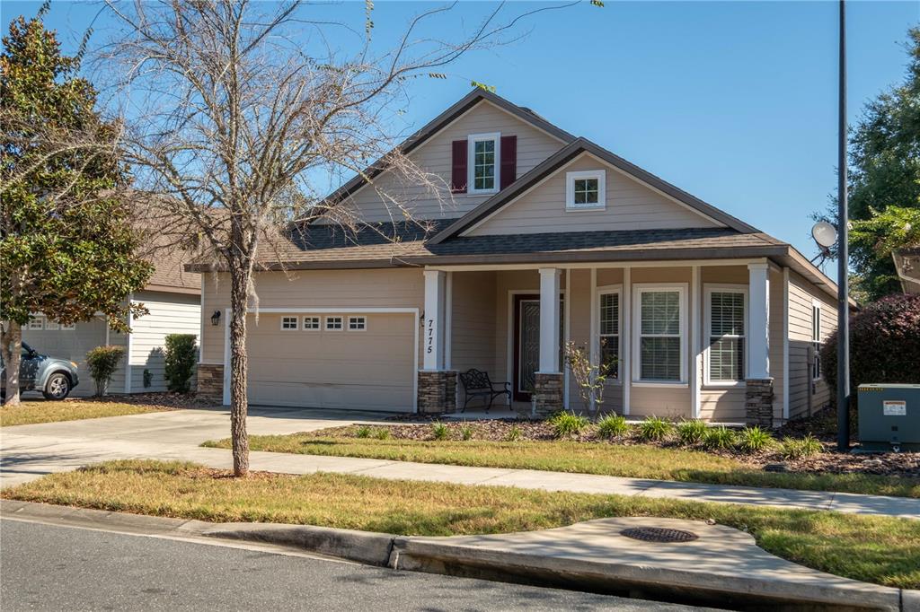 A single-story tan house with a two-car garage, front porch, and stone accents — 7775 SW 80TH DRIVE, GAINESVILLE, FL