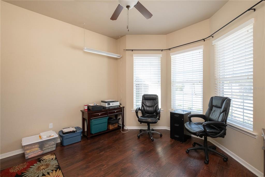 A home office features dark wood flooring, a bay window with blinds, and two chairs — 7775 SW 80TH DRIVE, GAINESVILLE, FL