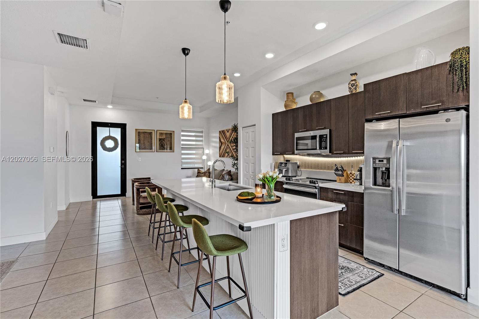 A modern kitchen features dark wood cabinetry, a white island with green stools, and stainless appliances — 8175 NW 104th Ave # 32, Doral FL 33178, DORAL, FL
