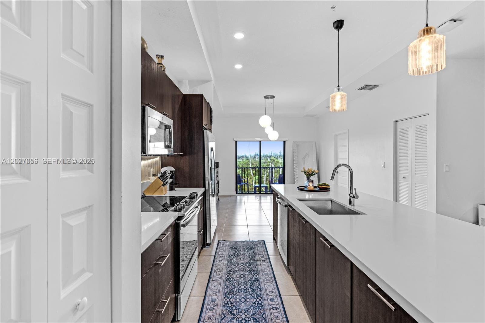 A modern kitchen features dark wood cabinetry, white countertops, and a view of a balcony — 8175 NW 104th Ave # 32, Doral FL 33178, DORAL, FL