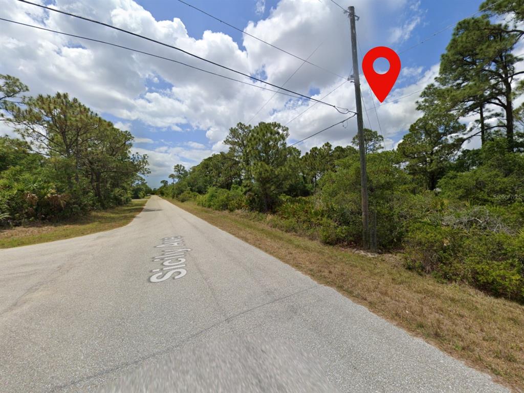 A paved road runs alongside a wooded lot with a utility pole and marker pin — 18090 SICILY AVENUE, PORT CHARLOTTE, FL