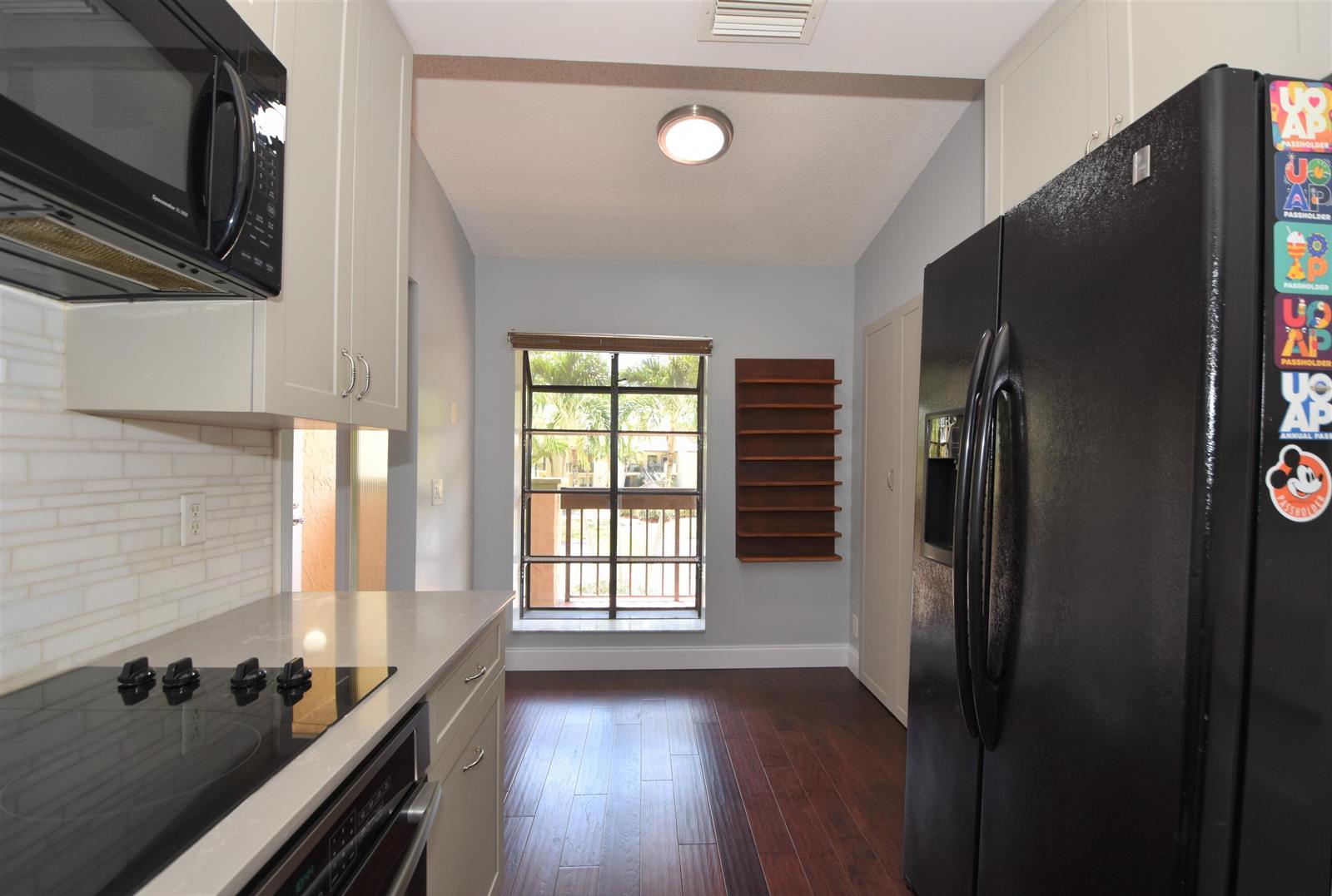 A kitchen features light cabinets, a black refrigerator, a glass stovetop, and a windowed balcony door — 5087 Oakhill Lane, Delray Beach FL 33484, DELRAY BEACH, FL