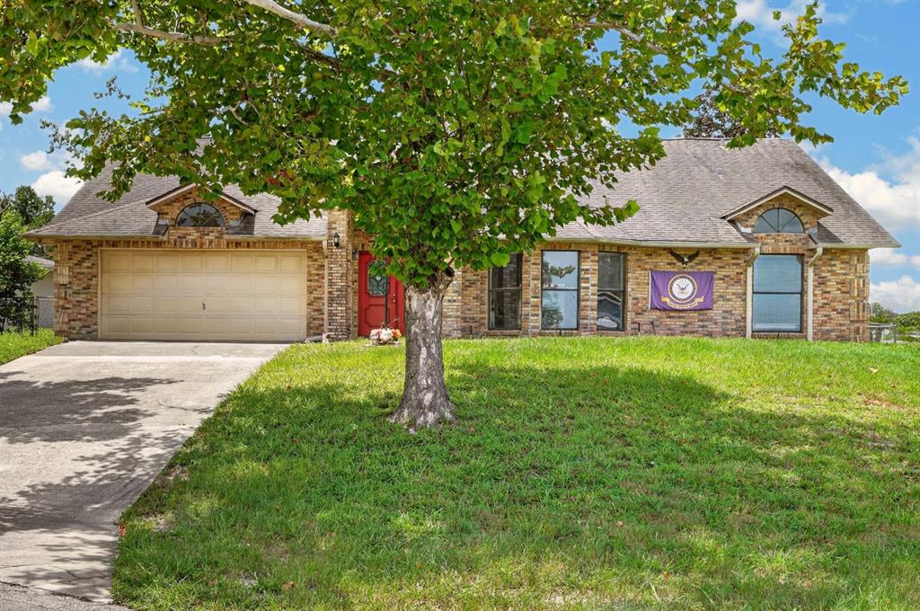 A single-story brick house with a two-car garage, a red front door, and a large tree — 1862 PORTVIEW AVENUE, DELTONA, FL