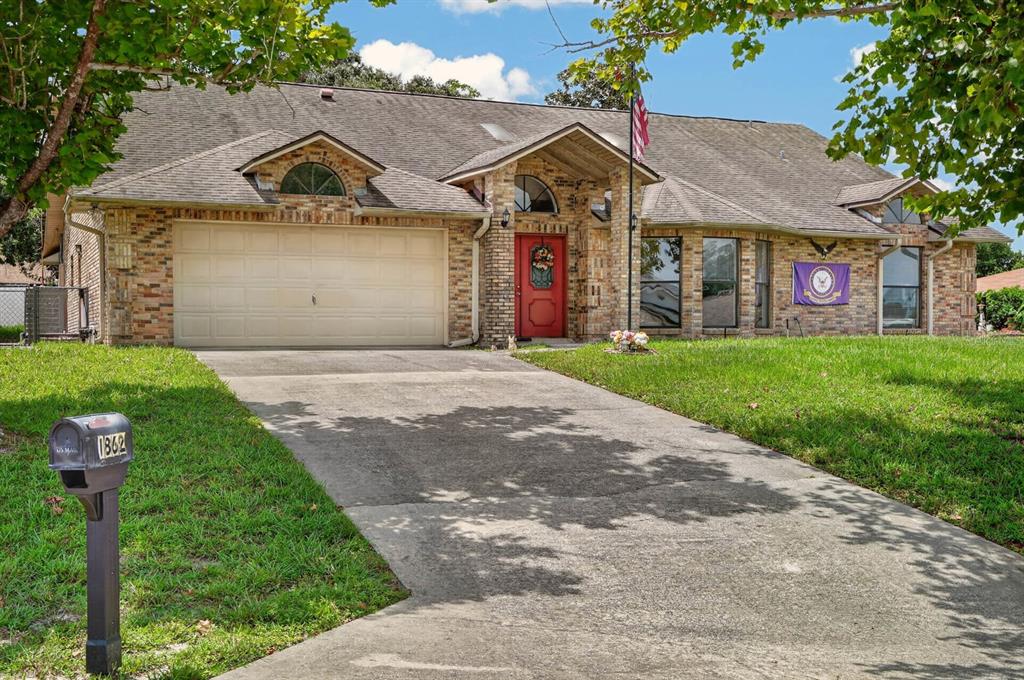 A single-story brick house with a two-car garage, red front door, and concrete driveway — 1862 PORTVIEW AVENUE, DELTONA, FL