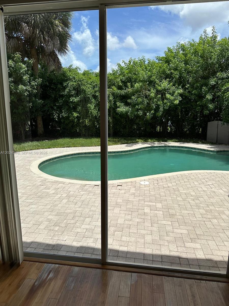 A view through a sliding glass door shows a backyard pool and brick patio — 11090 Baybreeze Way, Boca Raton FL 33428, BOCA RATON, FL