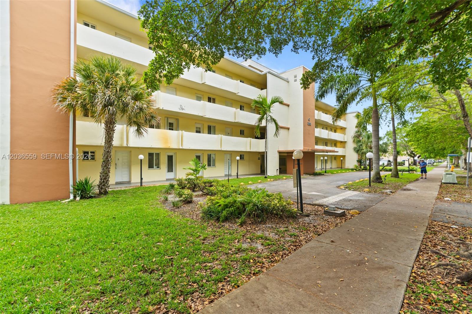A multi-story apartment building features yellow exterior walls, balconies, and a palm-lined front lawn — 1201 NE 191st St # G219, Miami FL 33179, MIAMI, FL