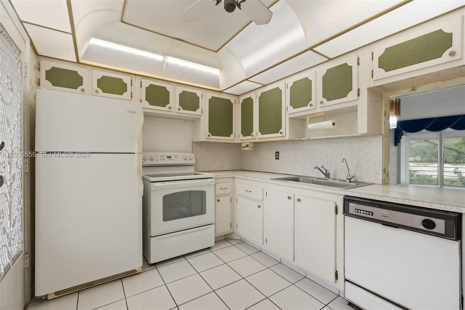A kitchen features white cabinets with green panels, white appliances, and white tiled flooring — 1201 NE 191st St # G219, Miami FL 33179, MIAMI, FL