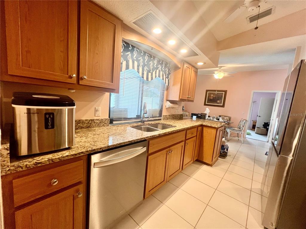 A kitchen features wood cabinets, granite countertops, stainless steel appliances, and light-colored tile flooring — 2132 ABSCOTT STREET, PORT CHARLOTTE, FL