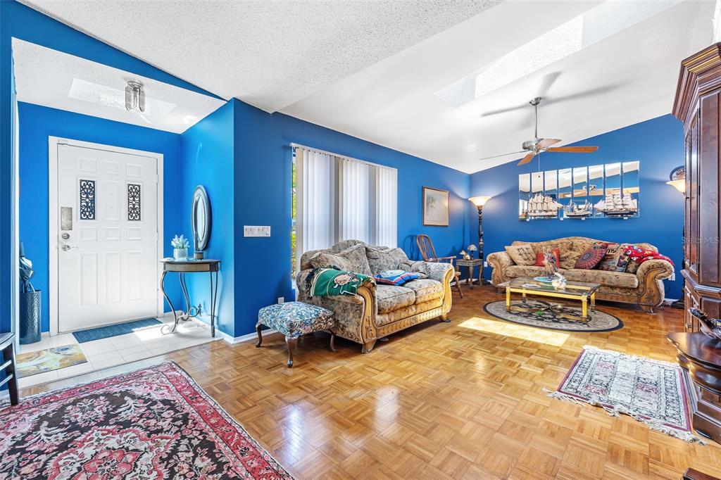 A living room with blue walls, parquet wood flooring, two patterned sofas, and a ceiling fan — 2132 ABSCOTT STREET, PORT CHARLOTTE, FL