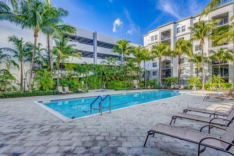 A rectangular swimming pool sits on a paved patio surrounded by palm trees and apartment buildings — 3110 Renaissance Way # 110, Boynton Beach FL 33426, BOYNTON BEACH, FL