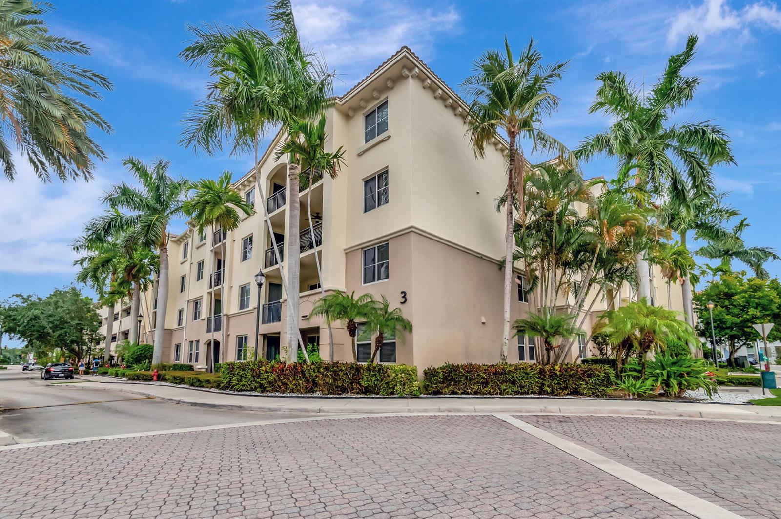 A multi-story apartment building with beige stucco walls and palm trees stands near a street — 3110 Renaissance Way # 110, Boynton Beach FL 33426, BOYNTON BEACH, FL