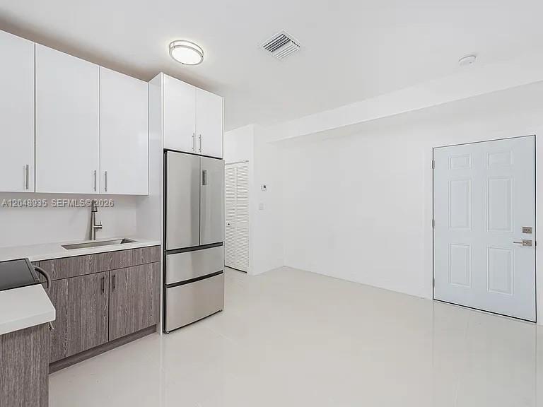 A kitchen features white upper cabinets, wood-grain lower cabinets, stainless steel appliances, and white floors — 676 NW 47th St # 8, Miami FL 33127, MIAMI, FL