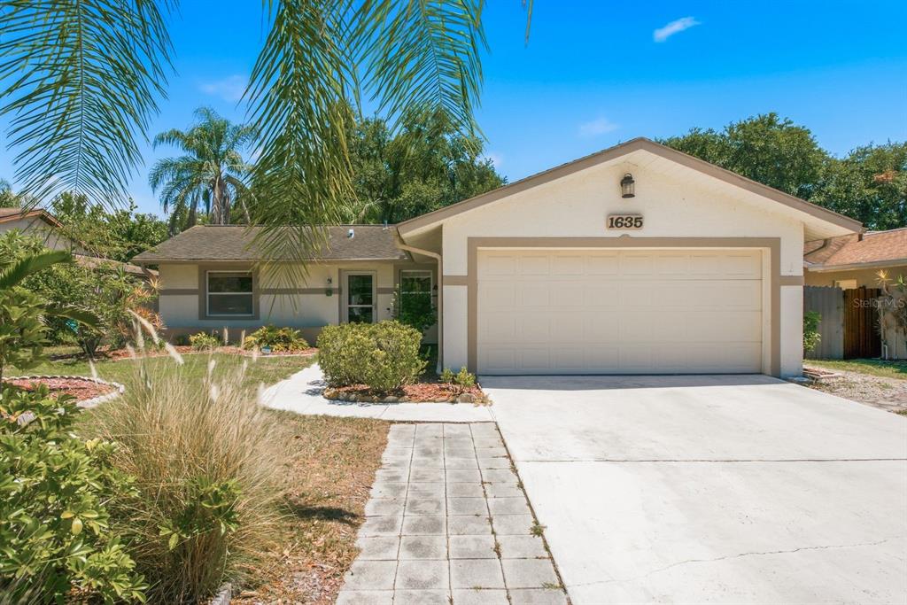 A single-story house with a beige stucco exterior, a two-car garage, and a concrete driveway — 1635 BRANDYWINE WAY, DUNEDIN, FL