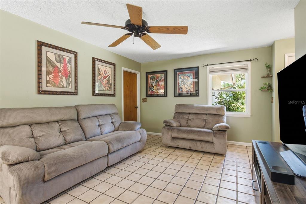 A living room features a grey sofa and armchair, tile flooring, and a ceiling fan — 1635 BRANDYWINE WAY, DUNEDIN, FL