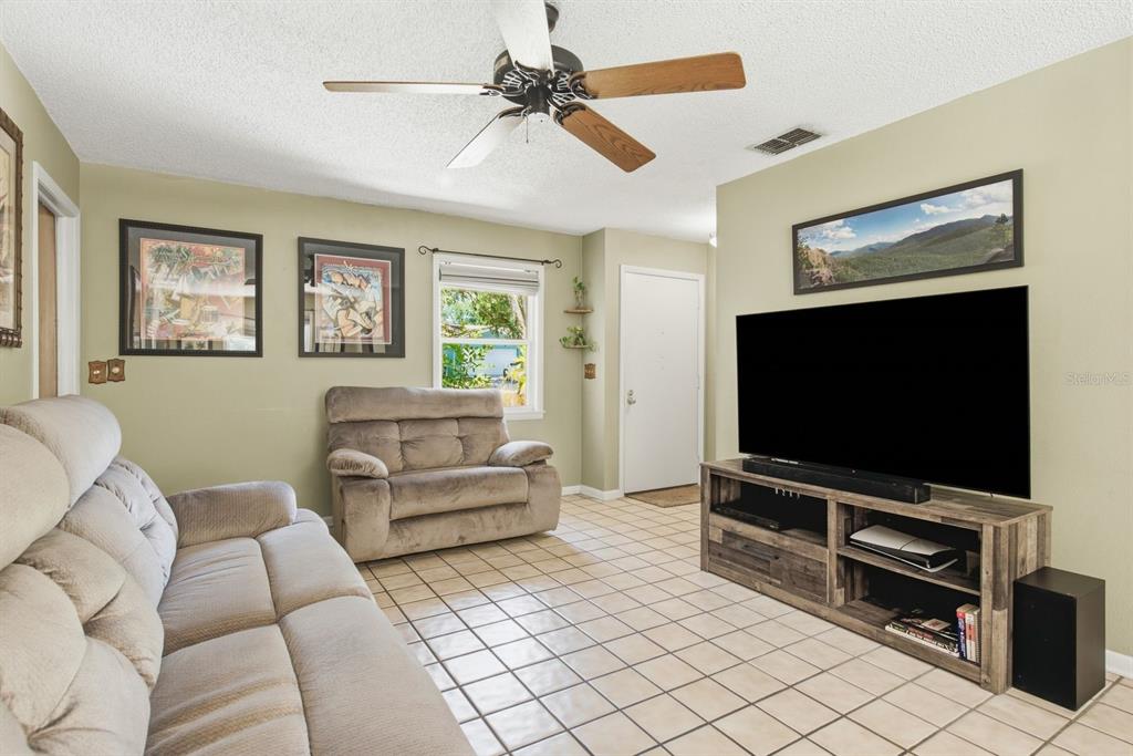A living room features light green walls, tiled floors, a ceiling fan, and a television — 1635 BRANDYWINE WAY, DUNEDIN, FL