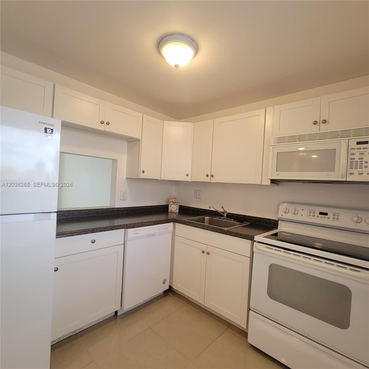 A kitchen features white cabinets, dark countertops, a white refrigerator, and a white stove — 6021 NW 61st Ave # 207, Tamarac FL 33319, TAMARAC, FL
