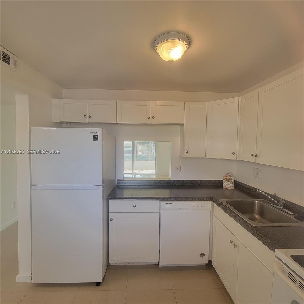 A kitchen features white cabinets, a white refrigerator, a dishwasher, and dark countertops — 6021 NW 61st Ave # 207, Tamarac FL 33319, TAMARAC, FL