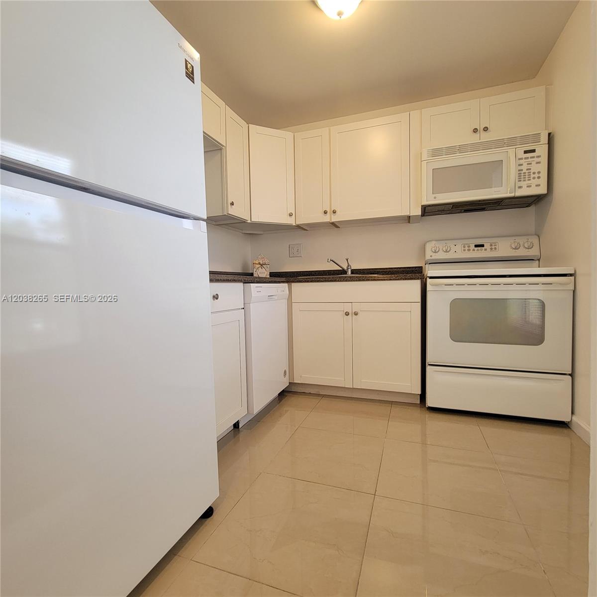 A kitchen features white cabinets, white appliances, and light-colored tile flooring — 6021 NW 61st Ave # 207, Tamarac FL 33319, TAMARAC, FL