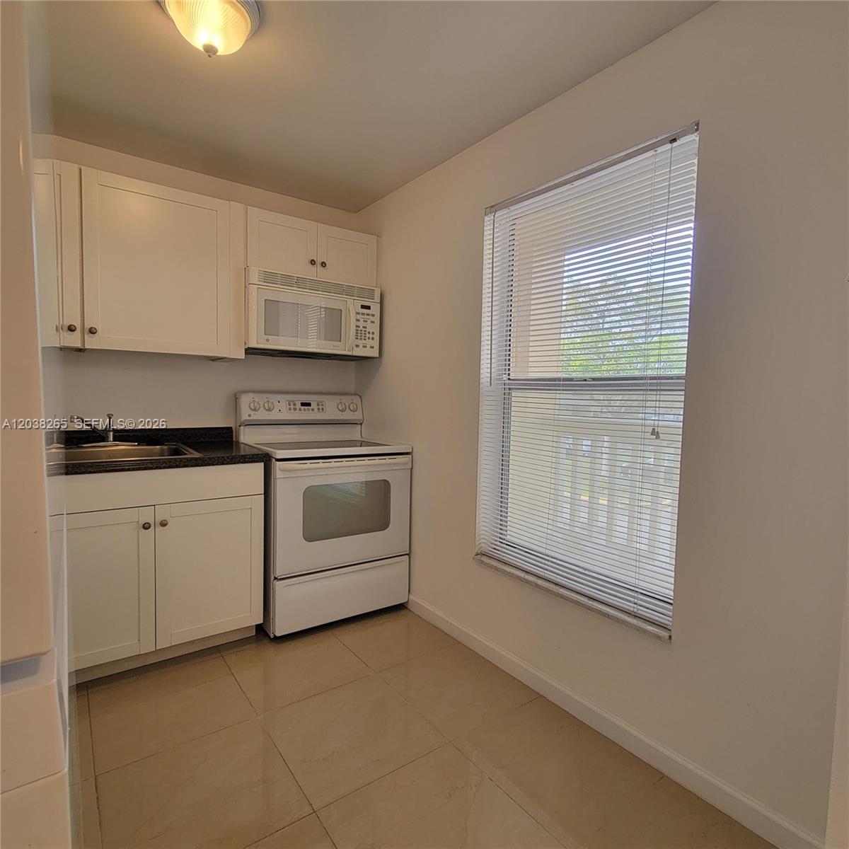 A small kitchen features white cabinets, white appliances, a dark countertop, and a window — 6021 NW 61st Ave # 207, Tamarac FL 33319, TAMARAC, FL