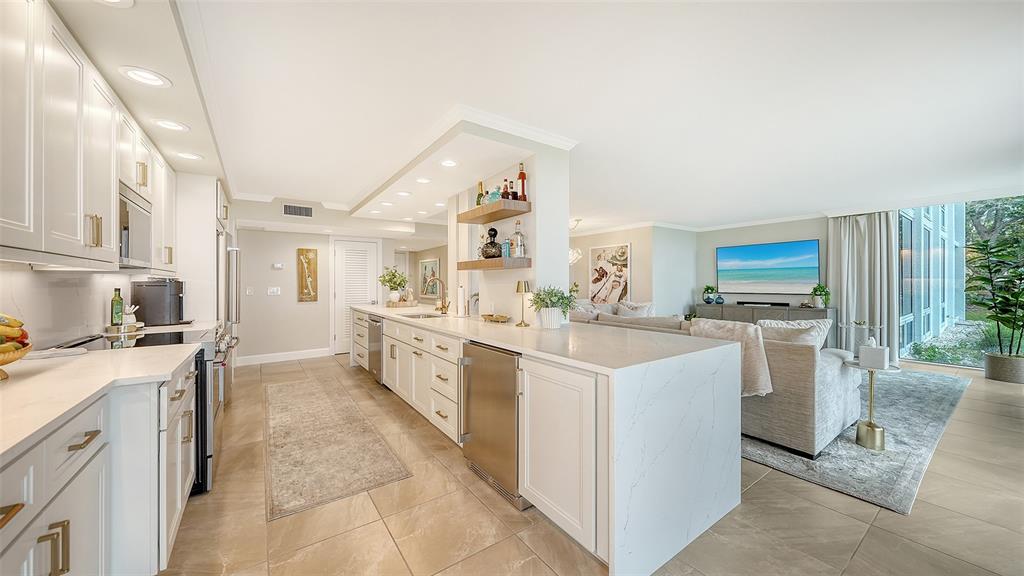 A modern kitchen with white cabinets and quartz countertops opens into a bright living area — 2425 GULF OF MEXICO DRIVE UNIT 1B, LONGBOAT KEY, FL