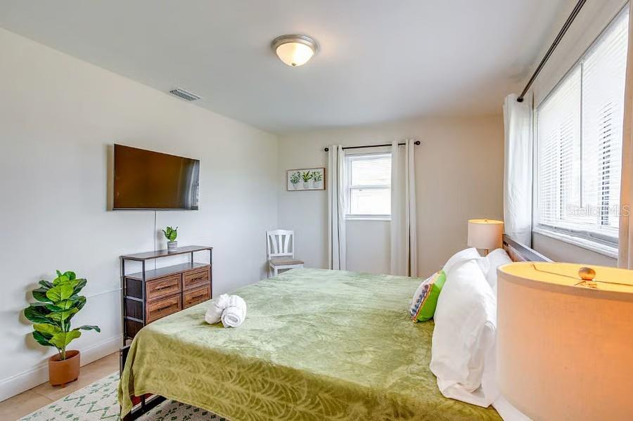 A bedroom features a bed with a green blanket, a wall-mounted television, and a dresser — 11533 69TH AVENUE, SEMINOLE, FL