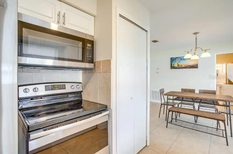 A kitchen with stainless steel appliances and white cabinets opens into a dining area — 11533 69TH AVENUE, SEMINOLE, FL