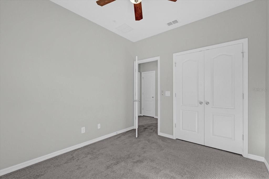 An empty bedroom features gray carpet, light gray walls, a ceiling fan, and white doors — 1148 PALMA VERDE PLACE, APOPKA, FL