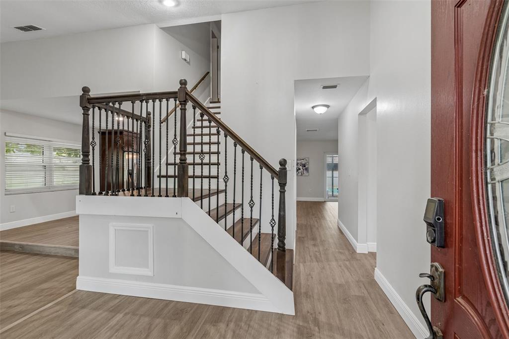 An entryway features a staircase with dark wood railings and light wood-look flooring — 16507 CRANWOOD PLACE, TAMPA, FL