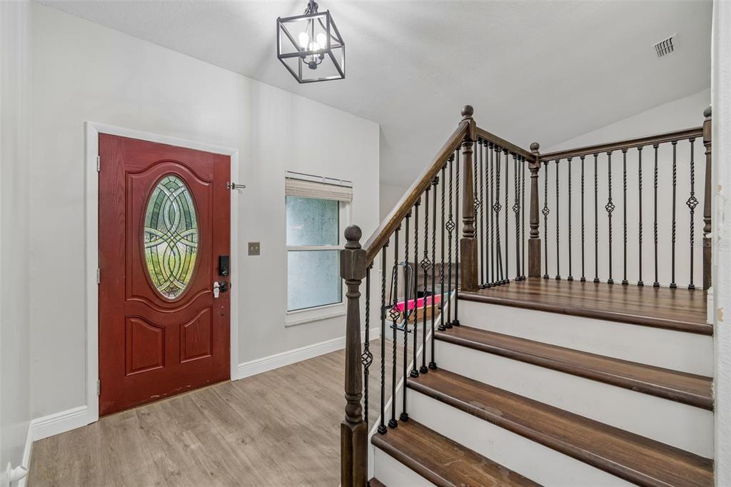 An entryway features a red front door, wood-look flooring, a staircase, and a geometric light fixture — 16507 CRANWOOD PLACE, TAMPA, FL