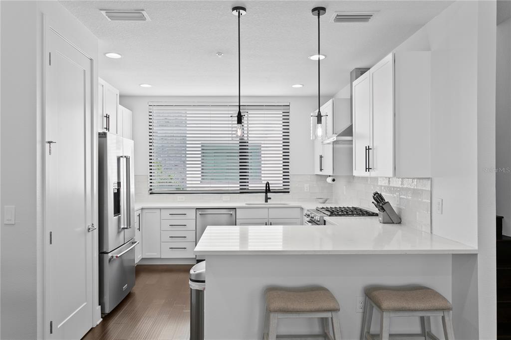 A modern white kitchen features stainless steel appliances, a peninsula with stools, and pendant lighting — 2511 N GRADY AVENUE UNIT 63, TAMPA, FL