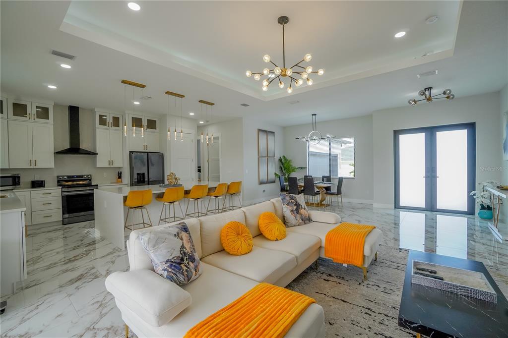 An open-concept living room and kitchen feature white cabinetry, marble-look flooring, and yellow accents — 15561 MELPORT CIRCLE, PORT CHARLOTTE, FL