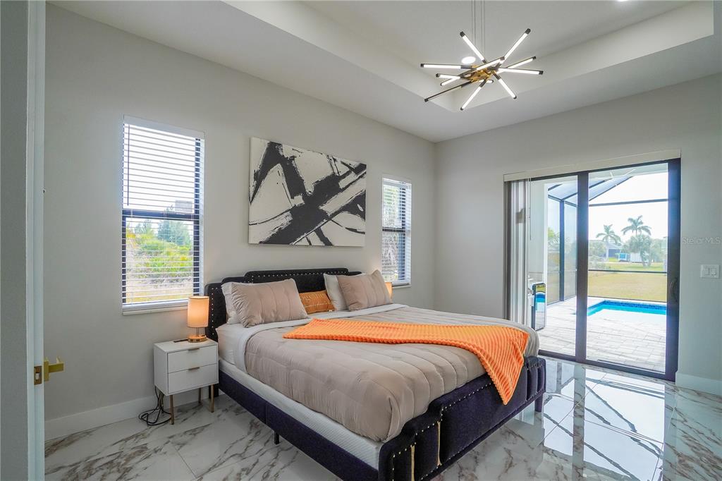 A modern bedroom features a tufted bed, marble floors, and sliding doors opening to a pool — 15561 MELPORT CIRCLE, PORT CHARLOTTE, FL