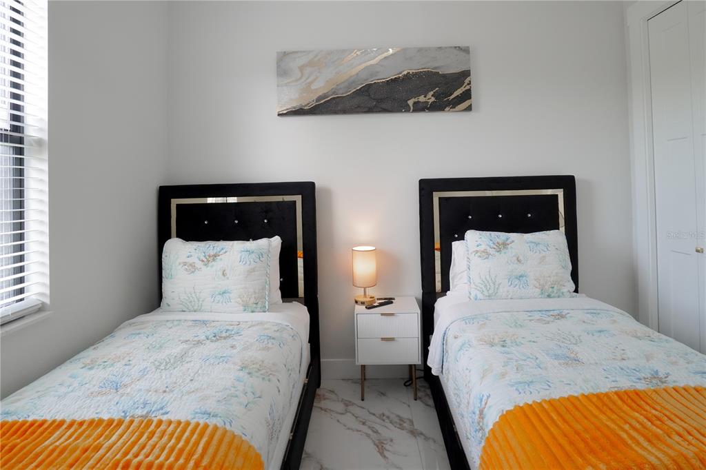 A bedroom features two twin beds with black headboards, a nightstand, and marble-look flooring — 15561 MELPORT CIRCLE, PORT CHARLOTTE, FL