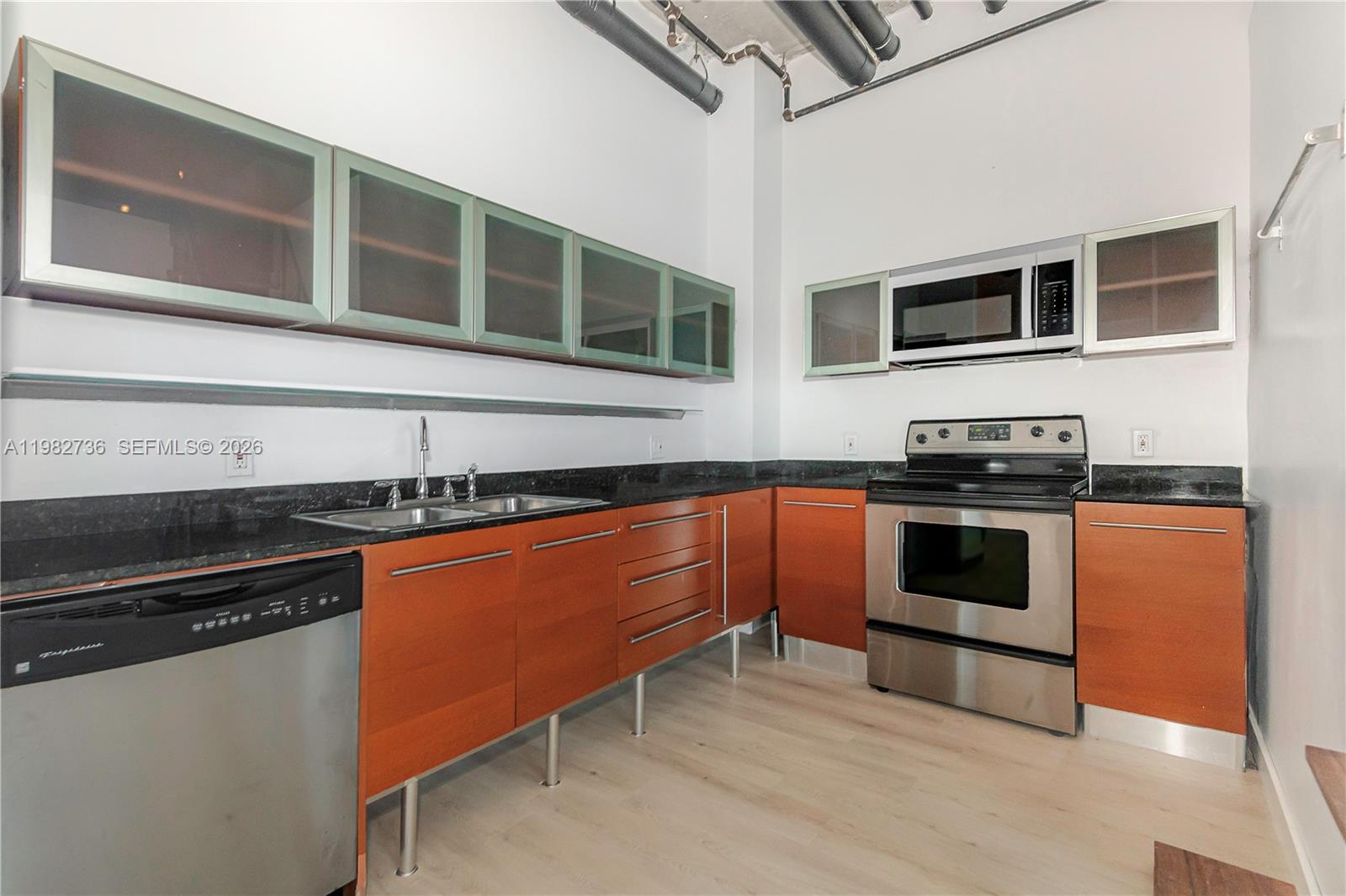 A kitchen features wood cabinets, stainless steel appliances, black countertops, and exposed industrial ceiling pipes — 10 SW South River Dr # 607, Miami FL 33130, MIAMI, FL
